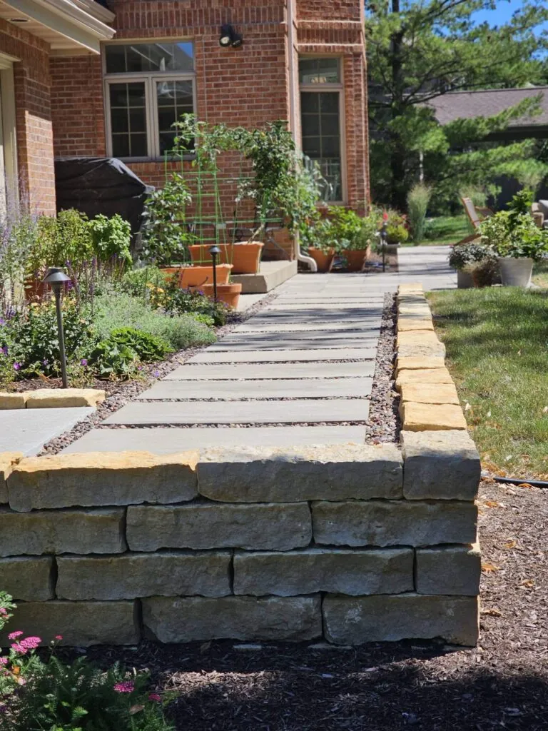 a paved pathway with a stone retaining wall, showcasing hardscape design alongside a brick house and garden in Middleton, WI